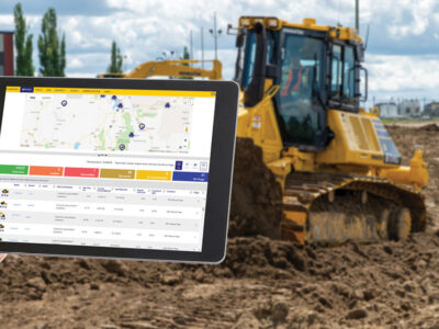 Hand holding tablet with software displayed and heavy construction equipment in background of photo
