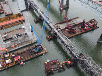 Installing one of two steel girders at Pier 7 with FRPD’s Peter D Anderson and Don Reid derricks. Protection Pier pile plicing underway in the background.