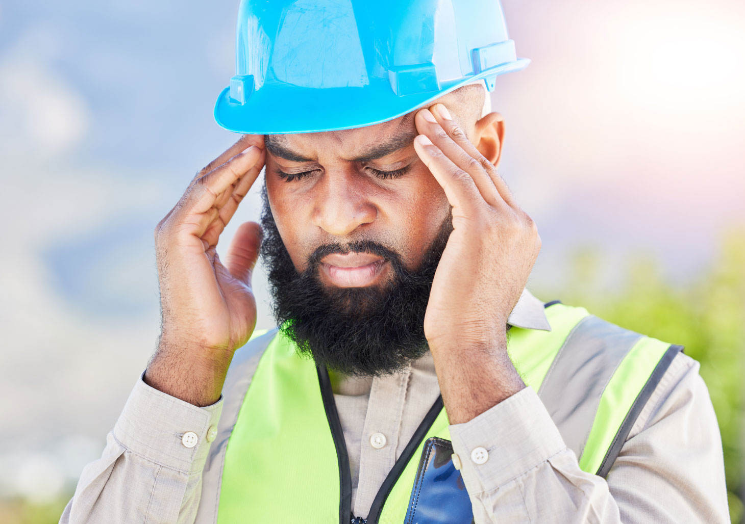 Man in blue hard hat rubbing temples