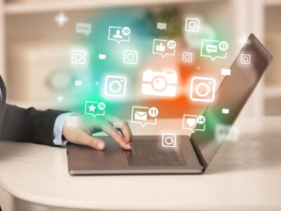 Graphic composition of hand typing on laptop with colourful icons hovering in the air above it