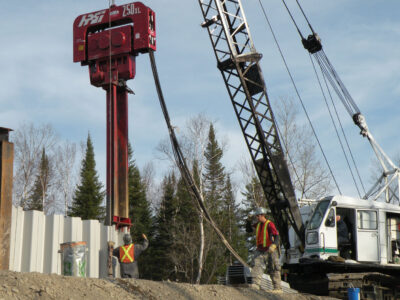 Workers operating heavy machinery driving sheet wall piles