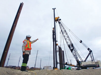 Fathi Mohamed wearing PPE, pointing at pile driving rig