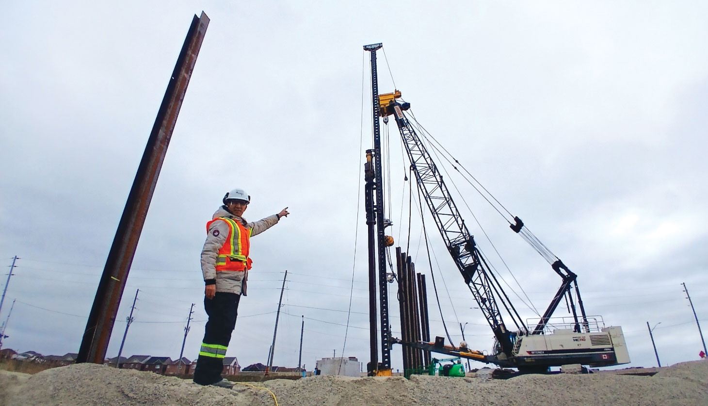 Fathi Mohamed wearing PPE, pointing at pile driving rig