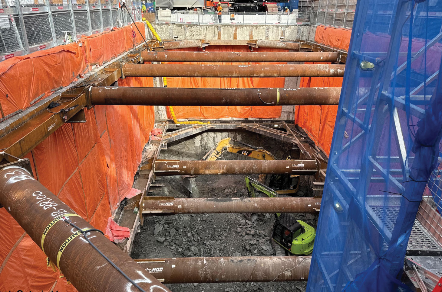 Excavators far below street level advance a shaft excavation (with shoring)