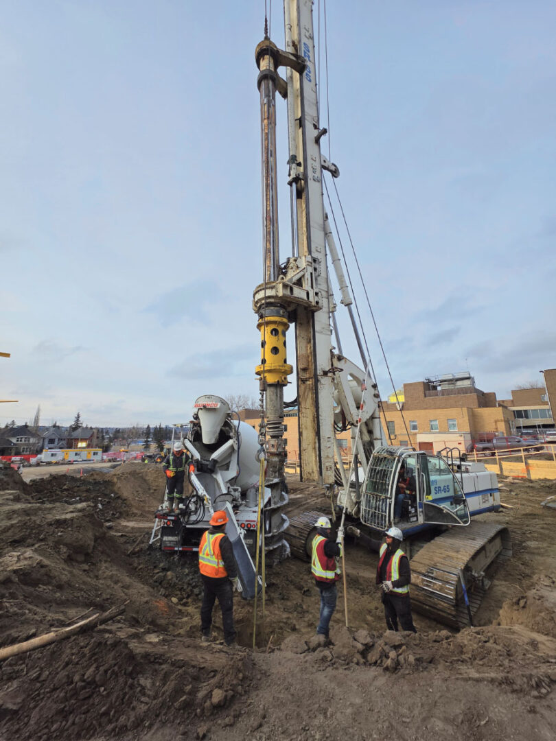Workers pouring cement with piling rig behind them