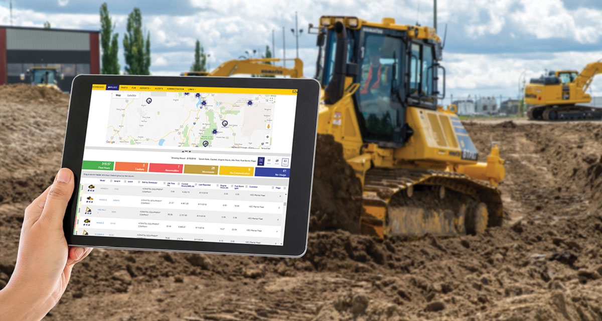 Hand holding tablet with software displayed and heavy construction equipment in background of photo