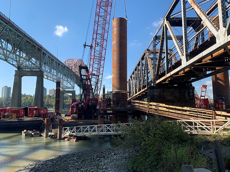 Large machinery hoisting section of pipe at Pier 10 downstream pile
