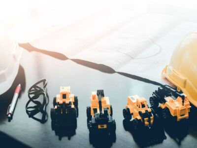 Toys of heavy machinery on a desk next to a hard hat