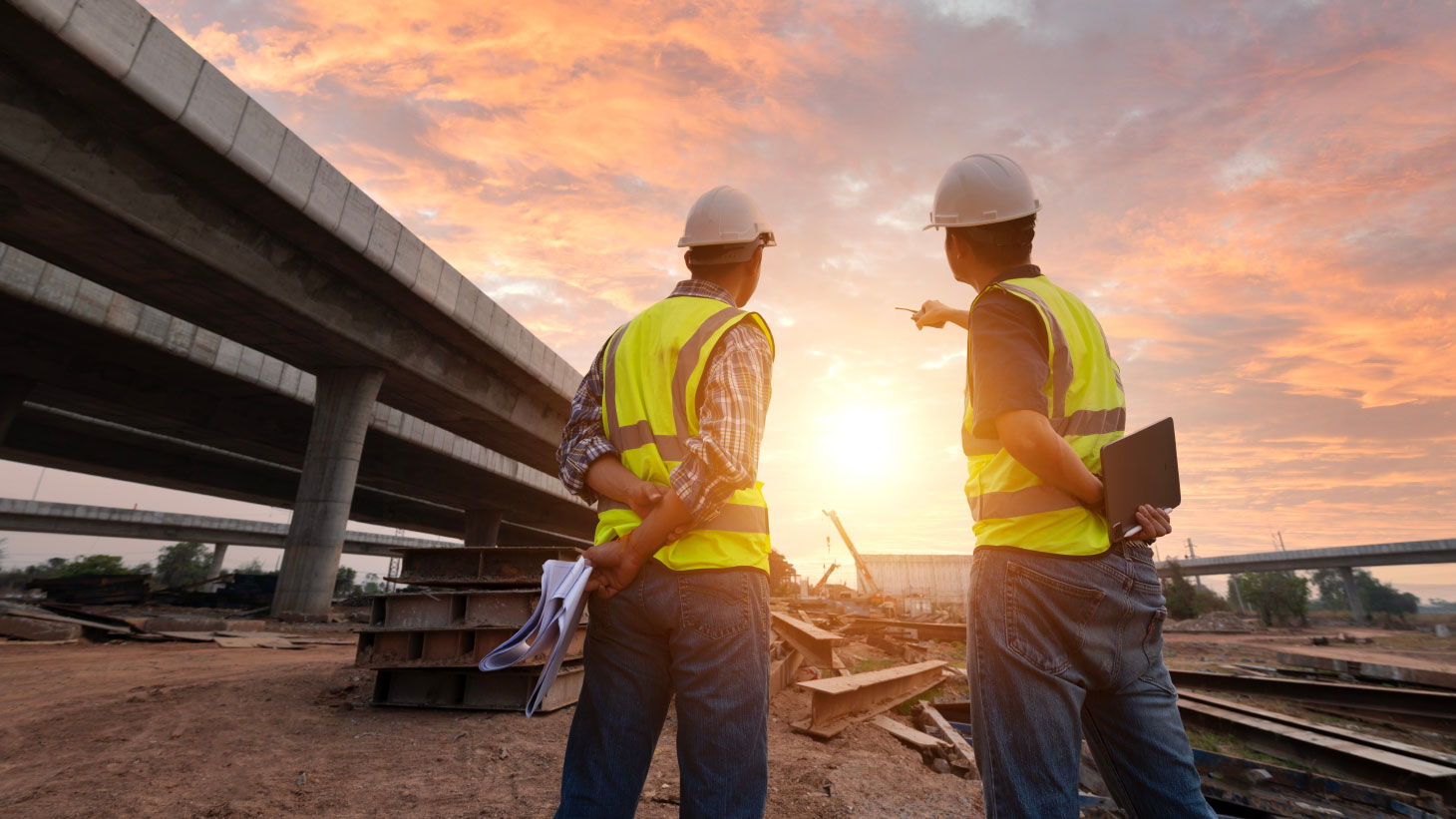 Two construction workers onsite, with sun setting in background