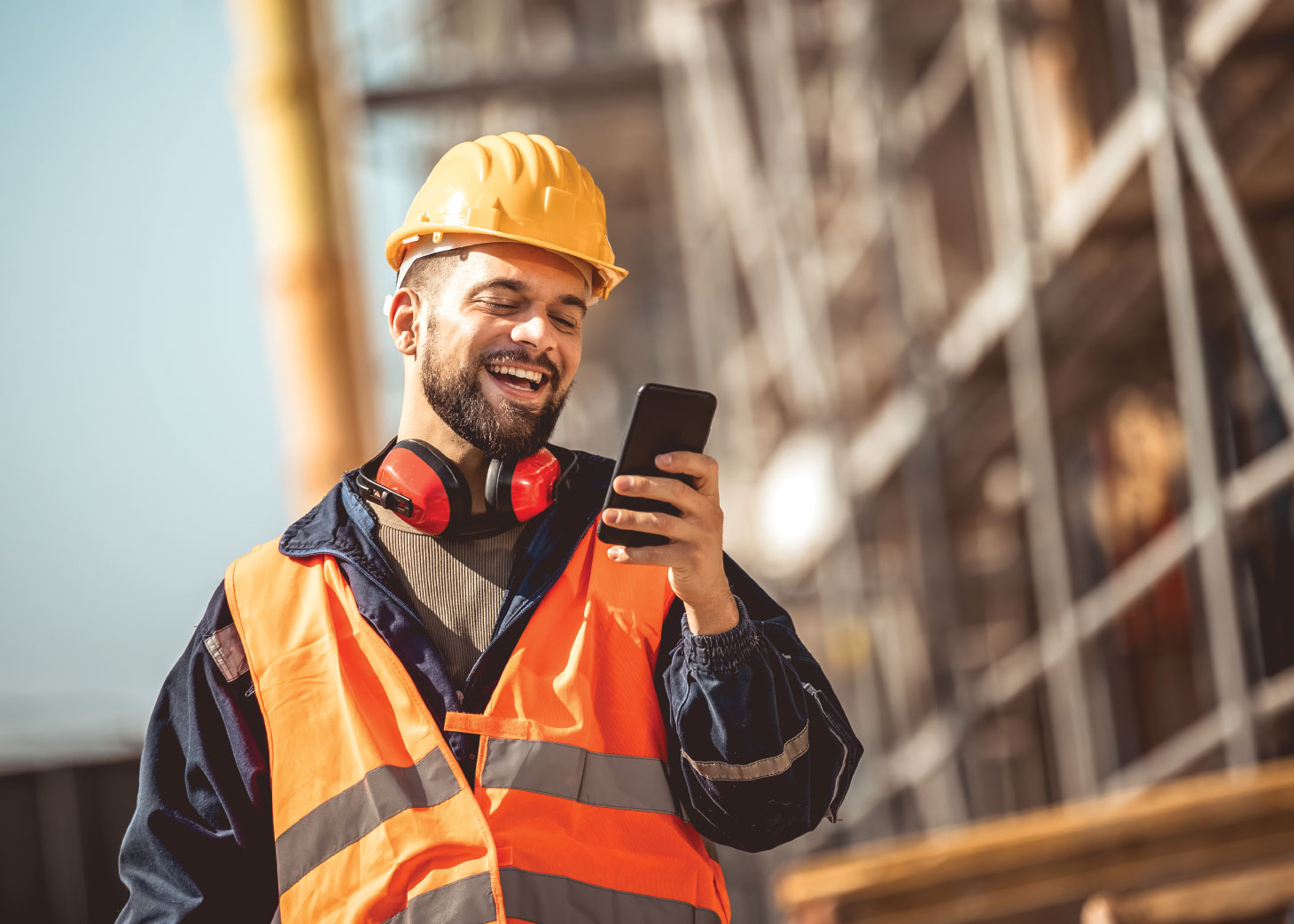 Un homme portant un gilet de sécurité et un casque, utilisant son téléphone sur un chantier de construction