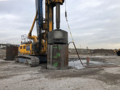 Heavy construction machinery driving a caisson into the ground