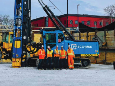 Group photo in front of blue, PRECO-MSE branded drilling rig // Photo de groupe devant une foreuse bleue de marque PRECO-MSE