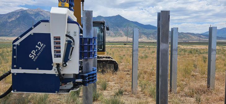 Pile cutter out in the field with mountain range in background